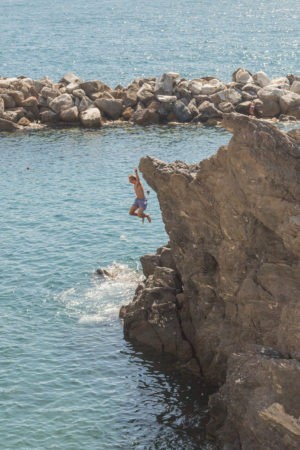 boy jumping from cliff in swimming area in manarola